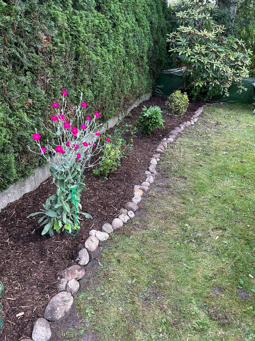 Fertiges Beet mit Rindenmulch und einer Kante aus Feldsteinen